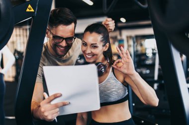 Erkek fitness spor salonu eğitmeni dinlenme ve genç çekici kadın ile gülümseyen egzersiz planı yaparken.