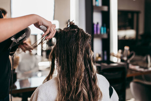 Beautiful brunette woman with long hair at the beauty salon getting a hair blowing. Hair salon styling concept.