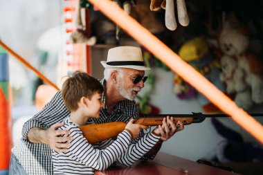 Büyükbaba ve torunu eğlenmek ve eğlence parkında birlikte iyi kaliteli zaman harcamak. Büyükbaba ödülü kazanmak için yardım ederken çocuk hava tabancası ile çekim. 