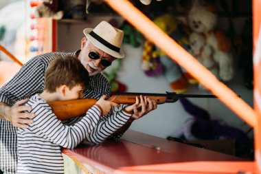 Büyükbaba ve torunu eğlenmek ve eğlence parkında birlikte iyi kaliteli zaman harcamak. Büyükbaba ödülü kazanmak için yardım ederken çocuk hava tabancası ile çekim. 