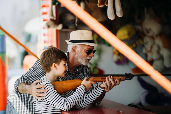 Büyükbaba ve torunu eğlenmek ve eğlence parkında birlikte iyi kaliteli zaman harcamak. Büyükbaba ödülü kazanmak için yardım ederken çocuk hava tabancası ile çekim. 