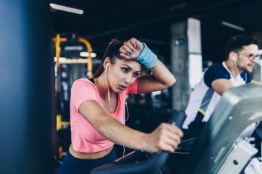 Spor salonunda bisiklet süren genç ve çekici bir kadın ve erkek. Bisiklet sürerken bacak egzersizi ve kardiyo egzersizi yapıyorlar..