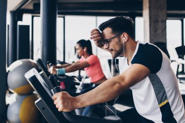 Spor salonunda bisiklet süren genç ve çekici bir kadın ve erkek. Bisiklet sürerken bacak egzersizi ve kardiyo egzersizi yapıyorlar..