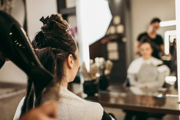 美容室で長い髪を持つ美しいブルネットの女性が髪を吹いて取得します ヘアサロンスタイリングのコンセプト — ストック写真