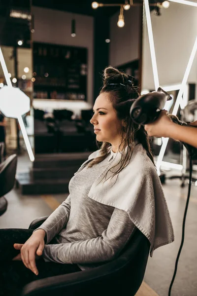 美容室で長い髪を持つ美しいブルネットの女性が髪を吹いて取得します ヘアサロンスタイリングのコンセプト — ストック写真