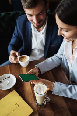 Modern kafe restoranında toplantı ya da öğle yemeği sırasında eski ahşap masa üzerinde boş yeşil ekranlı akıllı cep telefonu tutan iş adamlarının görüntüsü..