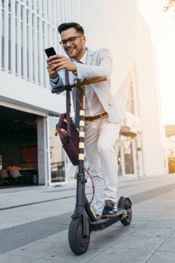 Şehir caddesinde elektrikli scooter kullanan ve kullanan genç modern bir adam. Modern ve ekolojik ulaşım kavramı.
