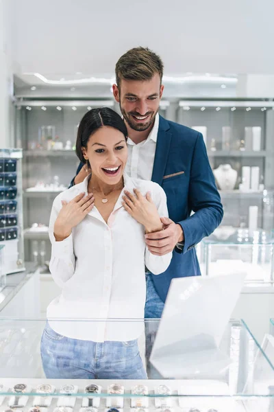 这对年轻漂亮的夫妇在现代珠宝店购物 年轻女子试穿华丽的项链和耳环 — 图库照片