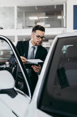 Galeride çalışan araba satıcısı ve araba detaylarını son kez kontrol ediyor alıcı gelmeden önce..