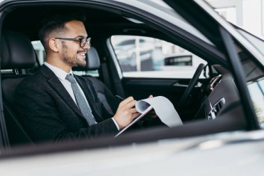 Galeride çalışan araba satıcısı ve araba detaylarını son kez kontrol ediyor alıcı gelmeden önce..