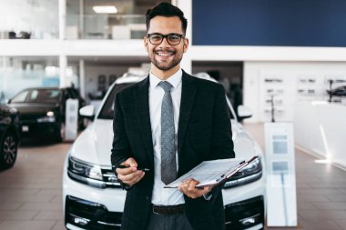 İyi görünümlü, neşeli ve samimi satıcı bir araba salonu veya showroom pozlar.