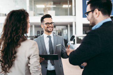 Araba galerisinden araba alan orta yaşlı bir çift. Araba satıcısı doğru karar vermelerine yardımcı oluyor..