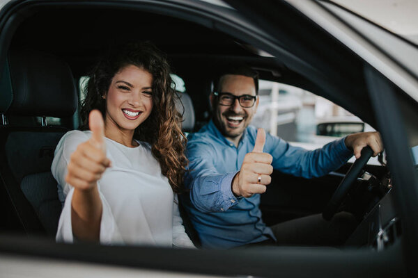 Happy middle age couple enjoying while choosing and buying new car at showroom.