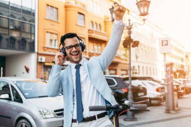Genç modern bir adam şehirde elektrikli scooter kullanıyor ve kullanıyor ve müzik dinliyor. Modern ve ekolojik ulaşım kavramı.