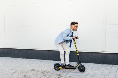 Şehir caddesinde elektrikli scooter kullanan ve kullanan genç modern bir adam. Modern ve ekolojik ulaşım kavramı.