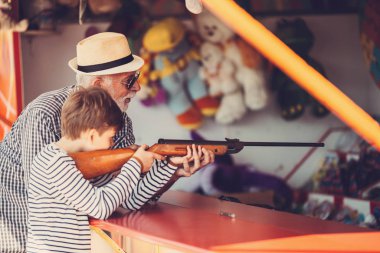 Büyükbaba ve torunu eğlenmek ve eğlence parkında birlikte iyi kaliteli zaman harcamak. Büyükbaba ödülü kazanmak için yardım ederken çocuk hava tabancası ile çekim. 