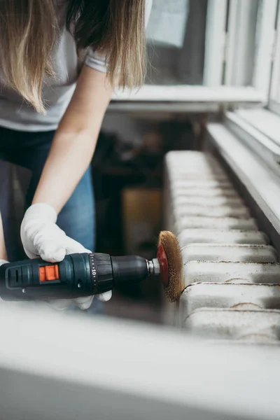 Beautiful and diligent middle age handy woman renovating her old home or apartment. She is holding professional grinder and brushing radiator for later painting. Do it yourself housework concept.