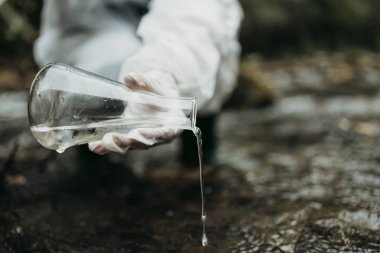Bilim adamı biyolog ve araştırmacı koruyucu takım kirli nehirden su örnekleri alarak yakın çekim.