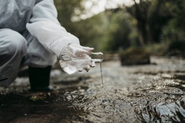 Bilim adamı biyolog ve araştırmacı koruyucu takım kirli nehirden su örnekleri alarak yakın çekim.