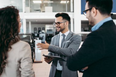 Araba galerisinden araba alan orta yaşlı bir çift. Araba satıcısı doğru karar vermelerine yardımcı oluyor..