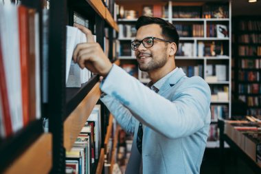 Orta yaşlı bir adam modern kitapçıda kitap seçiyor ve okuyor..