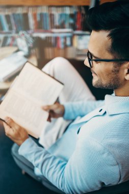 Orta yaşlı bir adam modern kitapçıda kitap seçiyor ve okuyor..