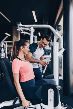 Modern spor salonunda spor yapan genç ve çekici bir kadın. Kişisel fitness hocası veya koçuyla birlikte..