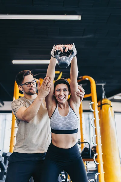 Young fit and attractive man and woman exercising workout with kettlebell in modern fitness gym.