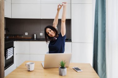 Çekici ve mutlu orta yaşlı serbest çalışan kadın evinde çalışıyor ve gülümsüyor. Arka planda modern mutfak. Serbest meslek kavramı.