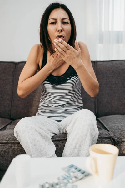 Sick and exhausted middle age woman suffering cough and flu fever. She sitting on sofa at her home.