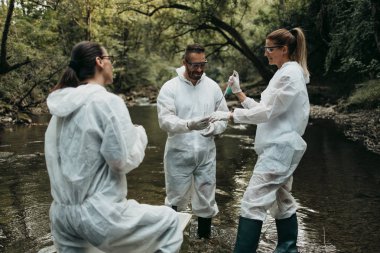 Scientists biologists and researchers in protective suits taking water samples from polluted river. clipart