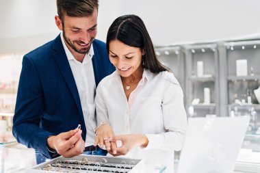 Modern kuyumcuda alışveriş yapan güzel bir çift. Pahalı bir yüzük ve bilezik takmış bir kadının elini yakın plan çek..