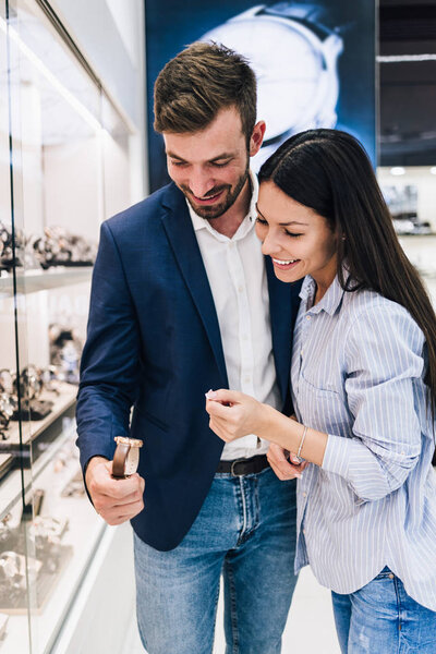 Beautiful couple enjoying in shopping at modern jewelry store. Close up shot of human hand holding expensive watch.
