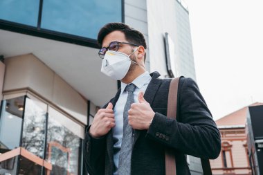 Şehir caddesinde koruyucu maskesiyle yürüyen bir iş adamı. Virüs salgını kavramı.