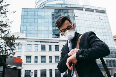 Şehir caddesinde koruyucu maskesiyle yürüyen bir iş adamı. Virüs salgını kavramı.