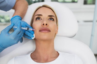 Çekici sarışın kadın güzellik kliniğinde gençleştirici yüz enjeksiyonu yaptırıyor. Güzellik uzmanı kadın kırışıklıklarını botulinyumla dolduruyor..