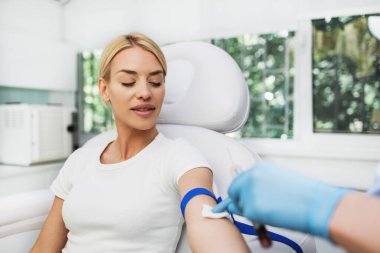 Beautiful young blond woman getting beauty treatment. Doctor taking blood samples from her arm. Platelet rich plasma PRP therapy process.	