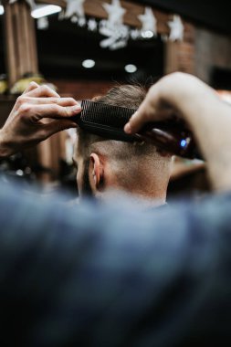 Yakışıklı bir genç adam saç ve sakal stili yaptırıyor ve profesyonel kuaför tarafından giydiriliyor..