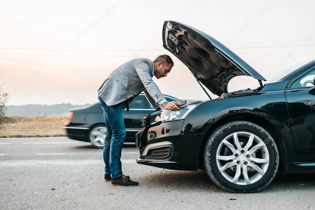 Elegant middle age business man trying to fix car breakdown or engine failure and waiting for towing service for help car accident on the road. Roadside assistance concept.