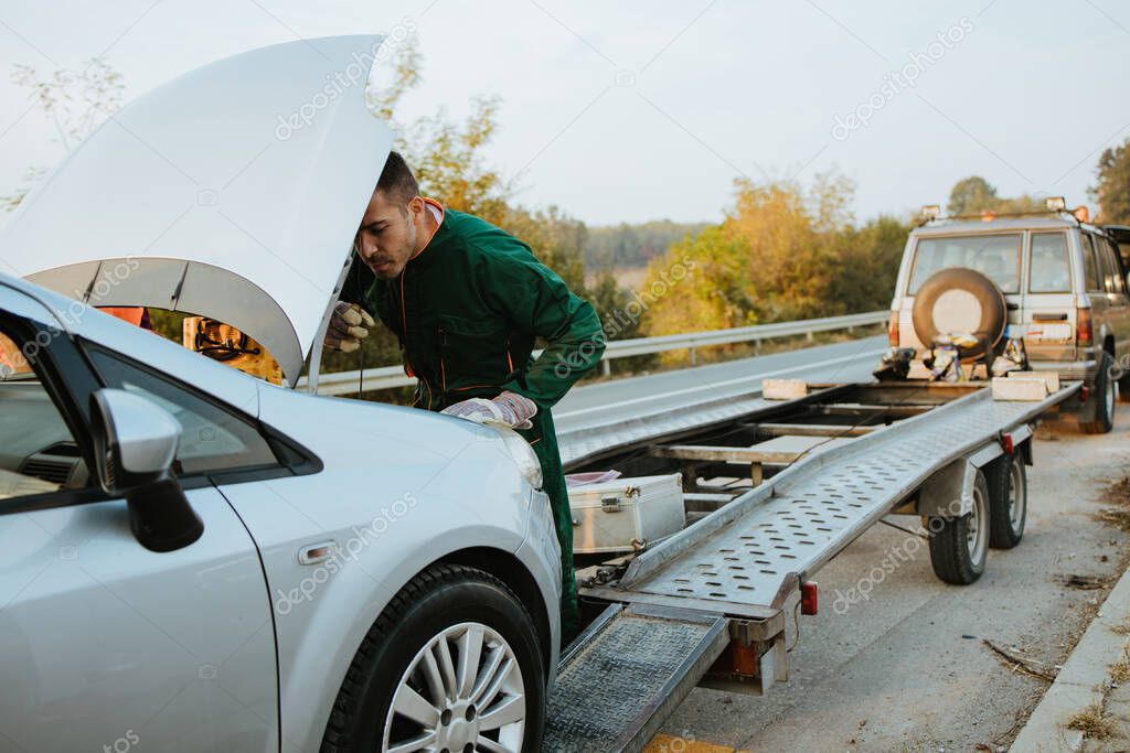 Two road assistant workers in towing service trying to start car engine with jump starter and energy station with air compressor. Roadside assistance concept.