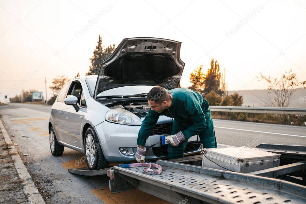 Road assistant worker in towing service trying to start car engine with jump starter and energy station with air compressor. Roadside assistance concept.
