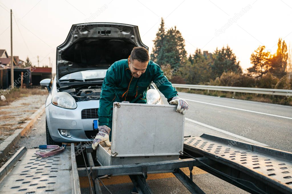 Road assistant worker in towing service trying to start car engine with jump starter and energy station with air compressor. Roadside assistance concept.
