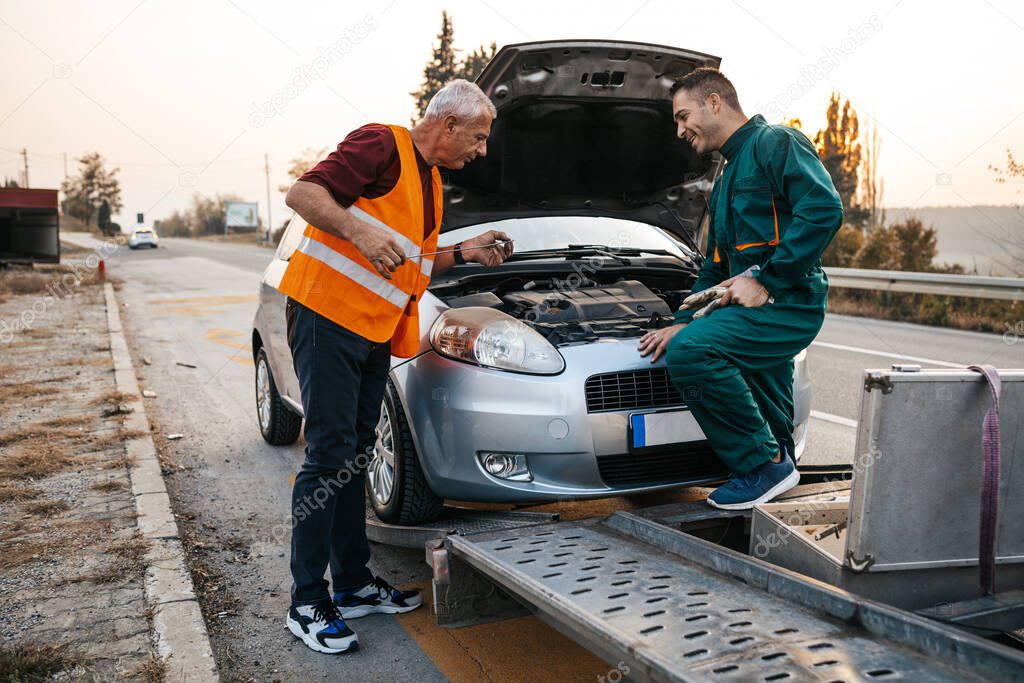 Two road assistant workers in towing service trying to fix car engine. They are checking oil engine level. Roadside assistance concept.