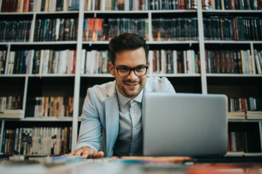 Genç, yakışıklı bir öğrenci ya da yazar pencerenin yanındaki üniversite kütüphanesinde oturuyor ve dizüstü bilgisayarı üzerinde çalışıyor. O ciddi ve yorgun. Güçlü ve derin gölgeleri olan doğal ışık. Arka planda kitap olan duvar.