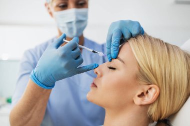 Çekici sarışın kadın güzellik kliniğinde gençleştirici yüz enjeksiyonu yaptırıyor. Güzellik uzmanı kadın kırışıklıklarını botulinyumla dolduruyor..