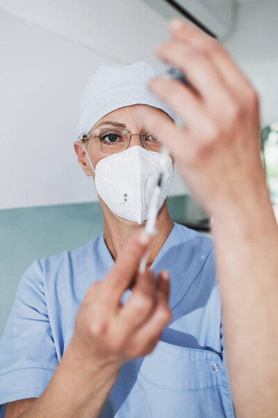 Close up shot of female doctor with face protective mask. She holding syringe. Selective focus on doctor's face.