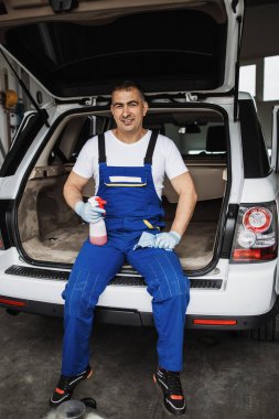 Araba yıkama işçisi lüks bir aracın önünde oturuyor ve poz veriyor. Araba temizleme, cilalama ve valelik hizmeti.