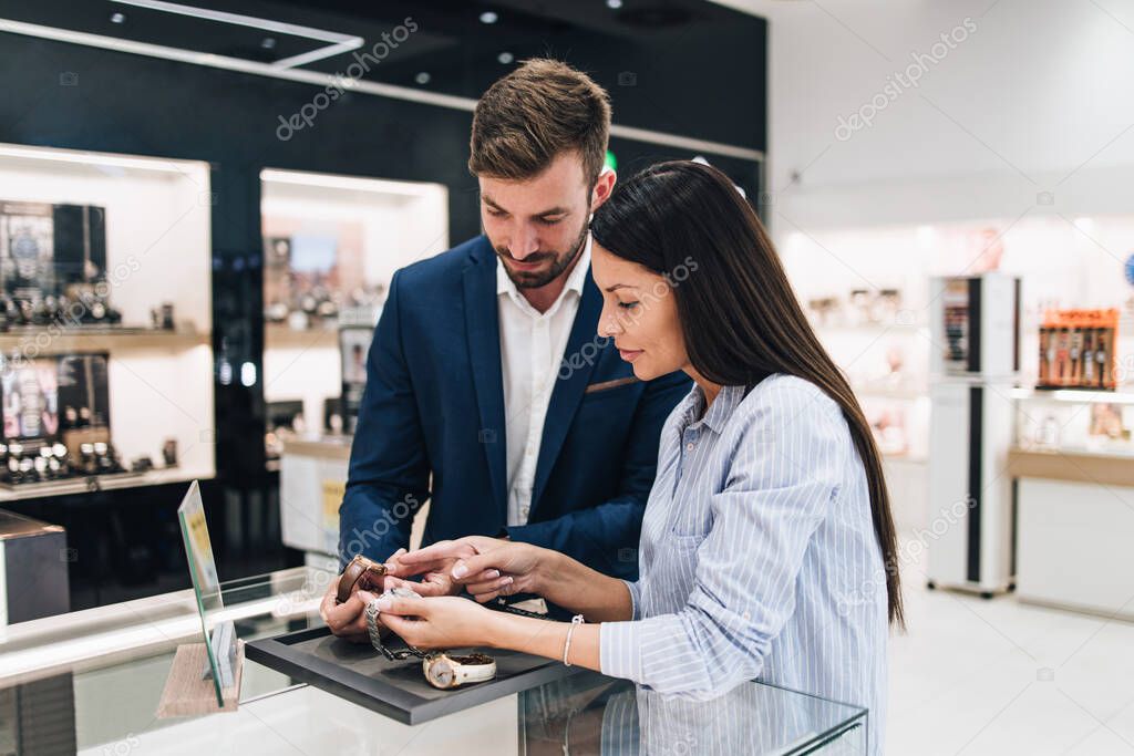 Beautiful couple enjoying in shopping at modern jewelry store. Close up shot of human hand holding expensive watch.