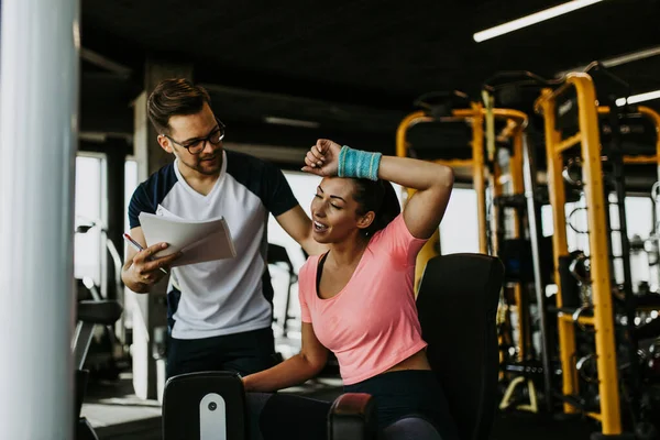 Modern spor salonunda spor yapan genç ve çekici bir kadın. Kişisel fitness hocası veya koçuyla birlikte..