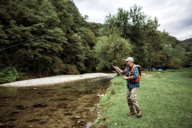 Kıdemli adam hızlı dağ nehrinde tek başına balık tutuyor. Aktif insanlar ve balıkçılık konsepti.